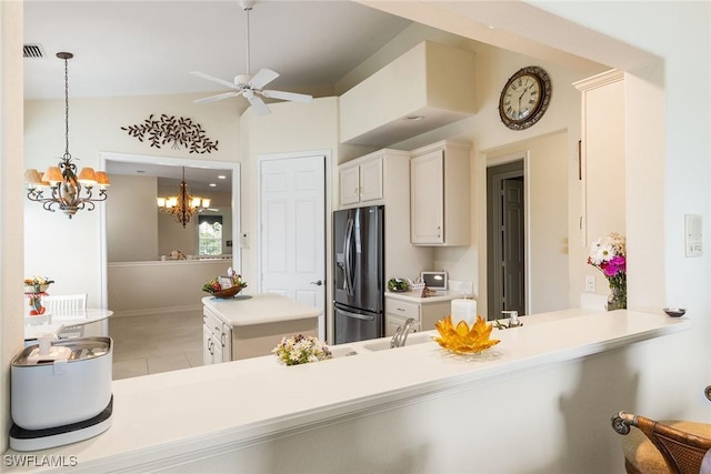 kitchen with light countertops, ceiling fan with notable chandelier, a peninsula, stainless steel refrigerator with ice dispenser, and light tile patterned flooring