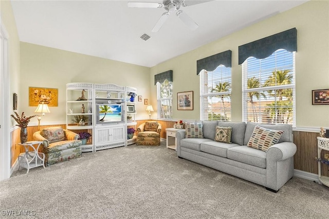 living area with visible vents, wood walls, carpet flooring, wainscoting, and a ceiling fan