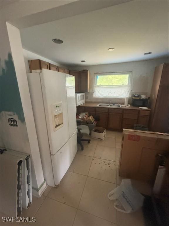 kitchen with light tile patterned flooring, white appliances, brown cabinetry, and a sink