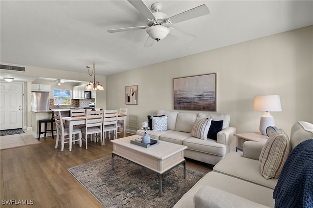 living room featuring visible vents, wood finished floors, and ceiling fan with notable chandelier