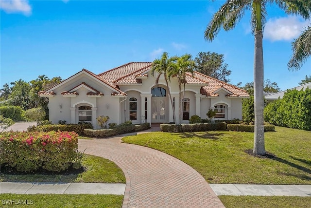 mediterranean / spanish home with stucco siding, curved driveway, a front yard, and a tiled roof