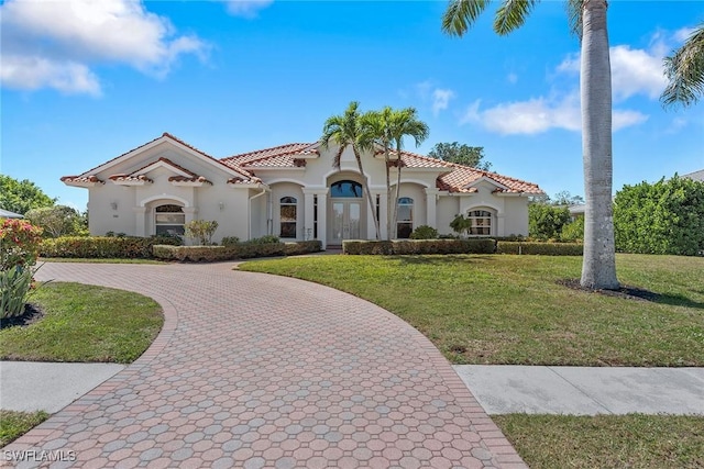 mediterranean / spanish-style house featuring stucco siding, a tiled roof, curved driveway, and a front yard