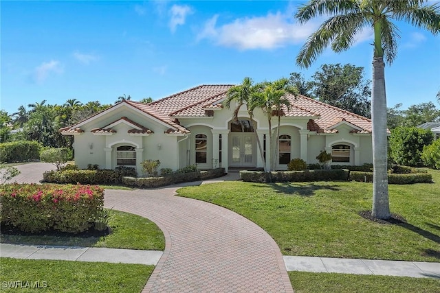 mediterranean / spanish house with a tile roof, stucco siding, a front lawn, and curved driveway