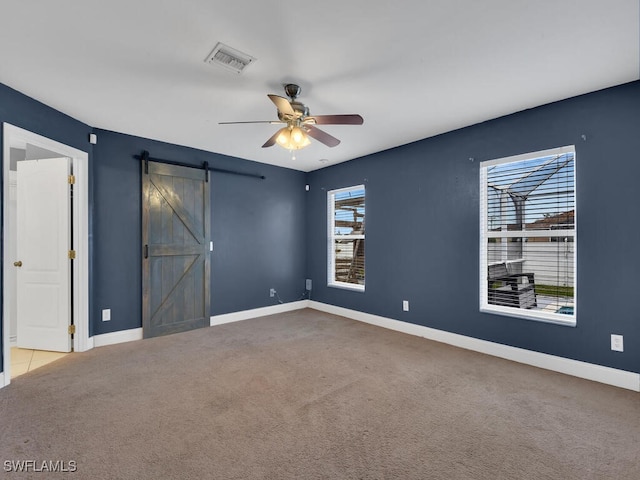 spare room featuring visible vents, baseboards, carpet, a barn door, and a ceiling fan