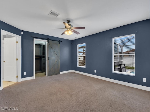 unfurnished bedroom with baseboards, a barn door, carpet floors, and visible vents