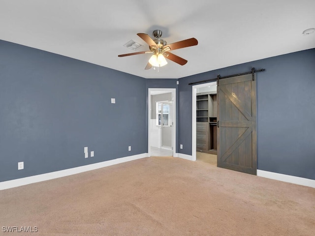 unfurnished bedroom featuring a barn door, baseboards, carpet floors, and visible vents