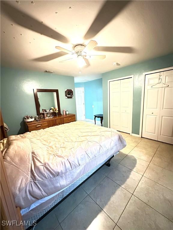 bedroom with visible vents, multiple closets, a ceiling fan, light tile patterned floors, and baseboards