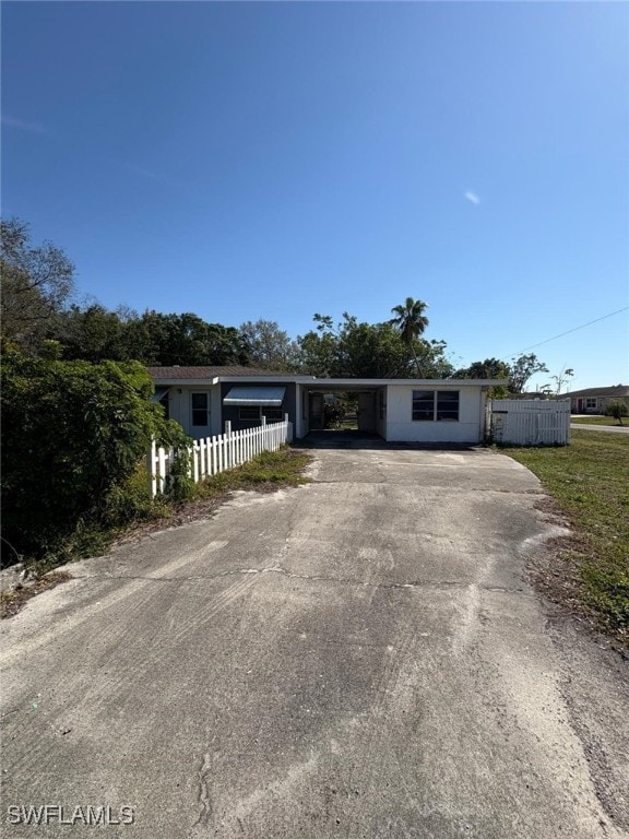 view of front of house with an attached carport, concrete driveway, and fence