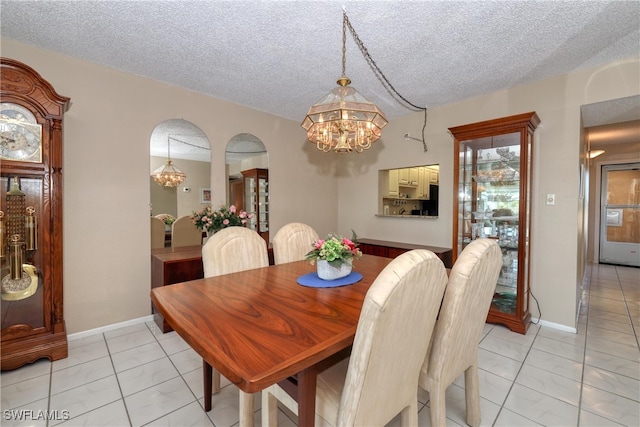 dining space featuring baseboards, light tile patterned floors, an inviting chandelier, arched walkways, and a textured ceiling