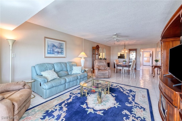 living room featuring light tile patterned floors, ceiling fan with notable chandelier, and a textured ceiling