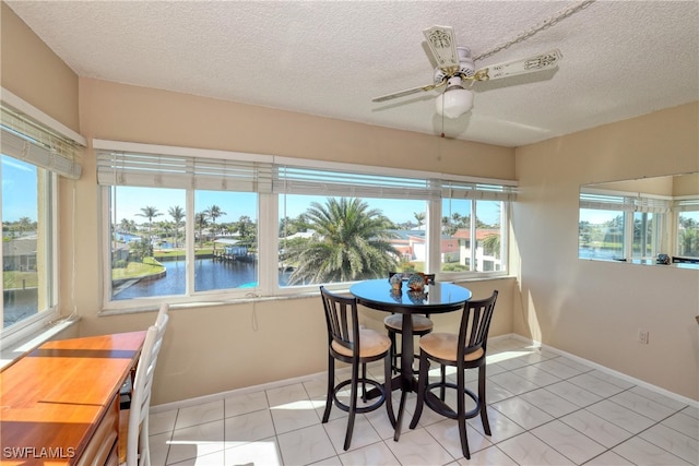 dining room featuring ceiling fan, baseboards, a water view, light tile patterned floors, and a textured ceiling