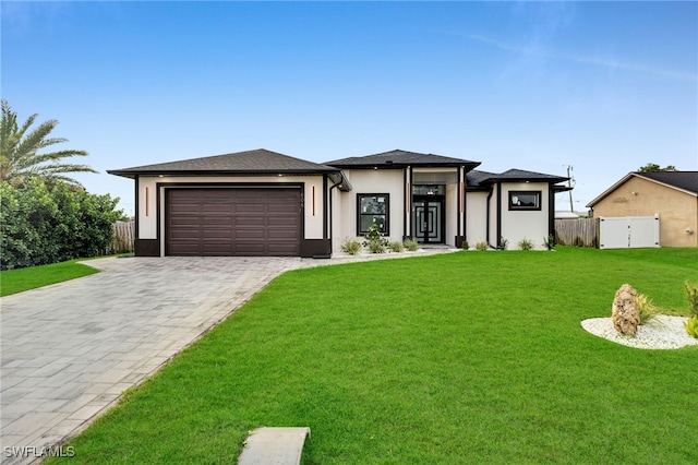 prairie-style house with a front lawn, fence, stucco siding, decorative driveway, and an attached garage