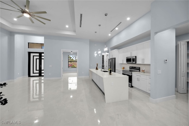 kitchen with a raised ceiling, appliances with stainless steel finishes, light countertops, and white cabinetry