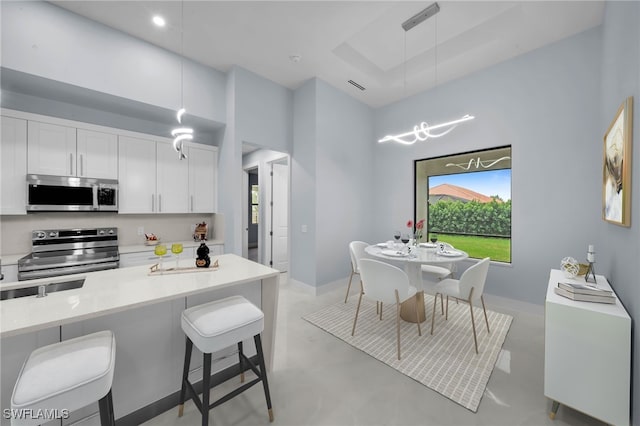 kitchen featuring pendant lighting, finished concrete flooring, appliances with stainless steel finishes, a breakfast bar area, and white cabinets