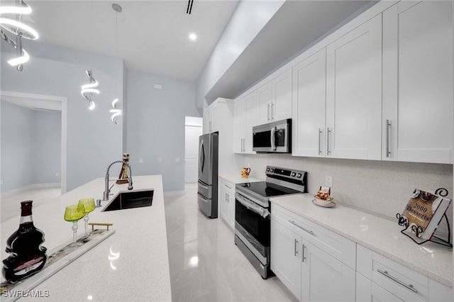 kitchen featuring light stone counters, a sink, hanging light fixtures, stainless steel appliances, and white cabinetry