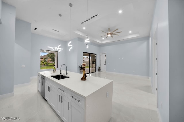 kitchen with visible vents, a center island with sink, a tray ceiling, a sink, and white cabinetry