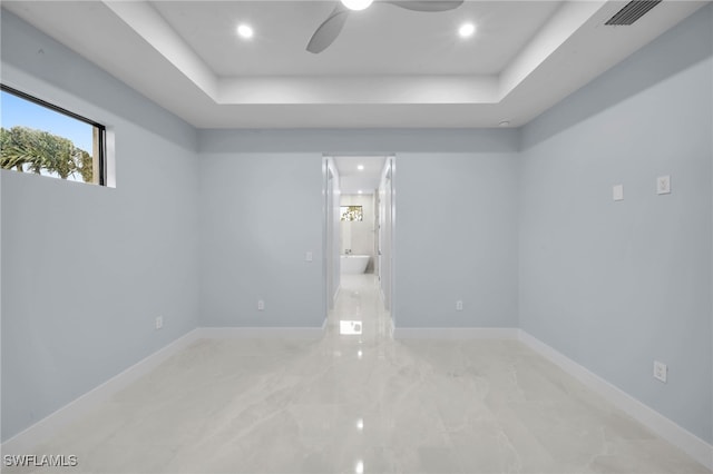 spare room featuring a tray ceiling, baseboards, visible vents, and ceiling fan