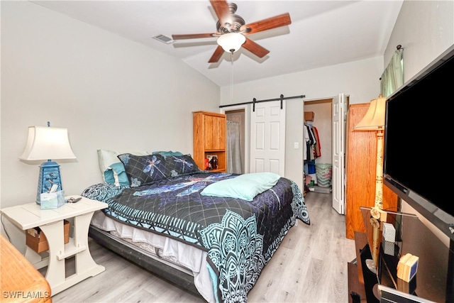 bedroom with light wood-type flooring, visible vents, a barn door, and a spacious closet