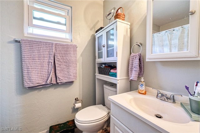 full bath with toilet, vanity, and a textured wall