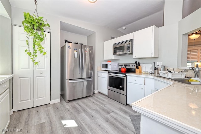 kitchen with light wood finished floors, light countertops, white cabinets, stainless steel appliances, and a sink