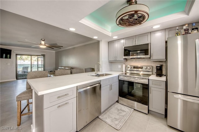 kitchen featuring a raised ceiling, a peninsula, gray cabinets, and appliances with stainless steel finishes