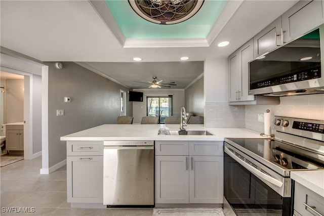 kitchen with gray cabinets, a sink, appliances with stainless steel finishes, a peninsula, and crown molding