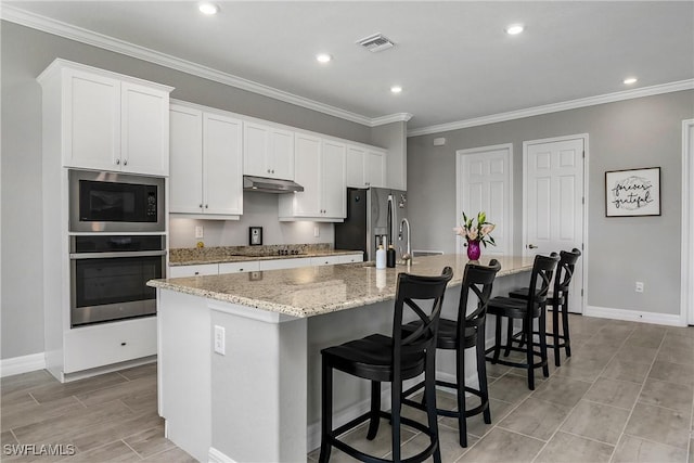 kitchen with stainless steel appliances, visible vents, a large island with sink, and white cabinetry