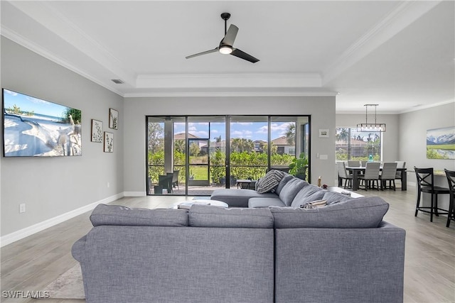 living room featuring visible vents, a raised ceiling, ornamental molding, ceiling fan with notable chandelier, and baseboards