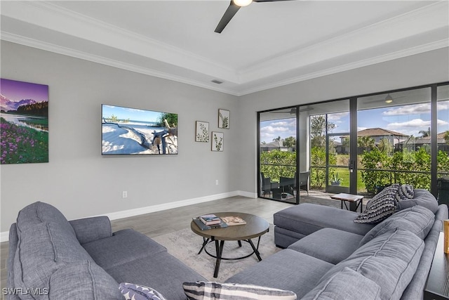 living area featuring wood finished floors, visible vents, baseboards, ornamental molding, and ceiling fan