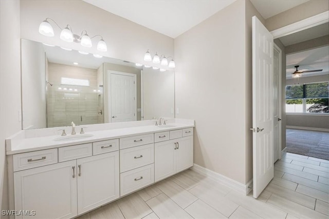 bathroom featuring a ceiling fan, baseboards, double vanity, a sink, and a shower stall