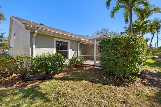 view of property exterior featuring glass enclosure, a lawn, and stucco siding