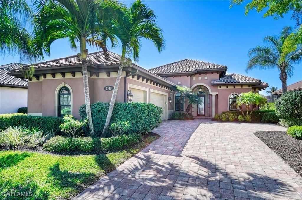 mediterranean / spanish home with decorative driveway, a tile roof, an attached garage, and stucco siding