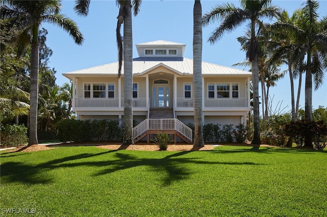 raised beach house featuring a porch, stairway, a front lawn, and metal roof