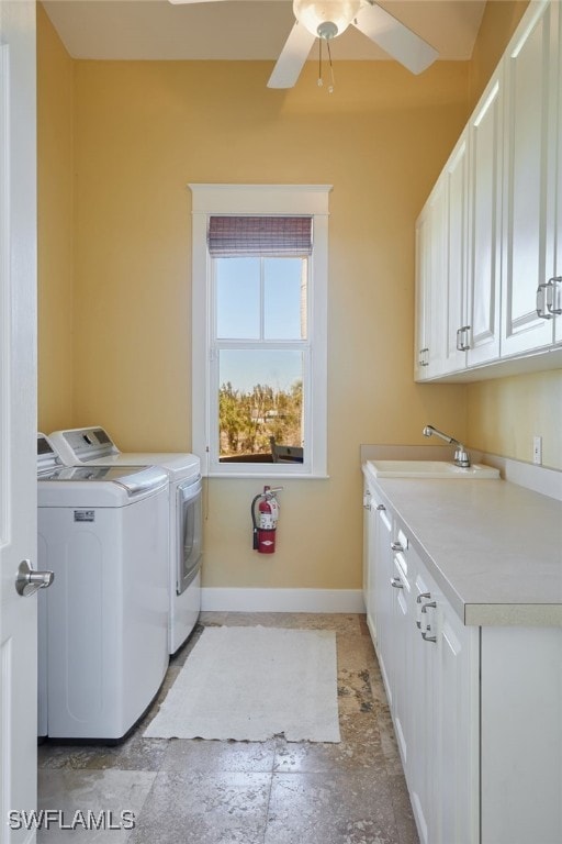 clothes washing area featuring baseboards, washer and clothes dryer, stone tile flooring, cabinet space, and a sink