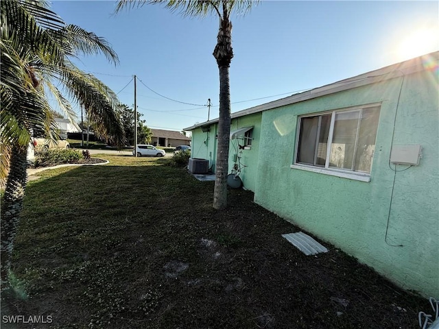 view of home's exterior with stucco siding, a lawn, and central AC