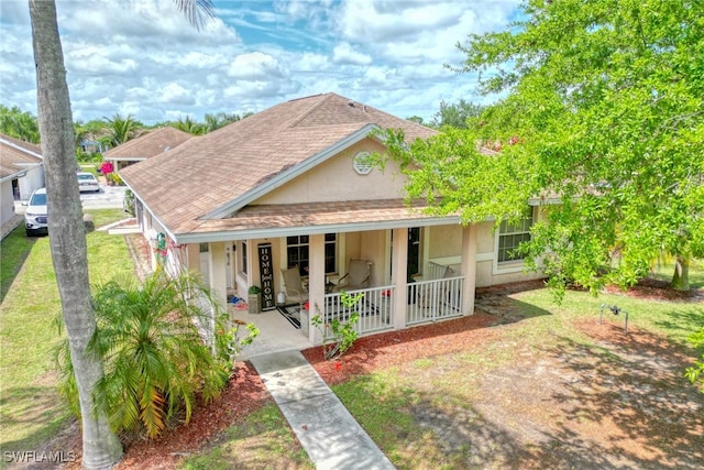 view of front of house with covered porch, stucco siding, a front yard, and roof with shingles