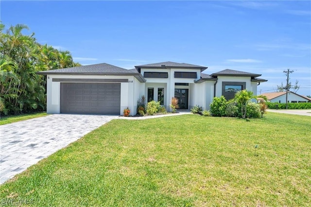 prairie-style home featuring decorative driveway, a front lawn, an attached garage, and stucco siding