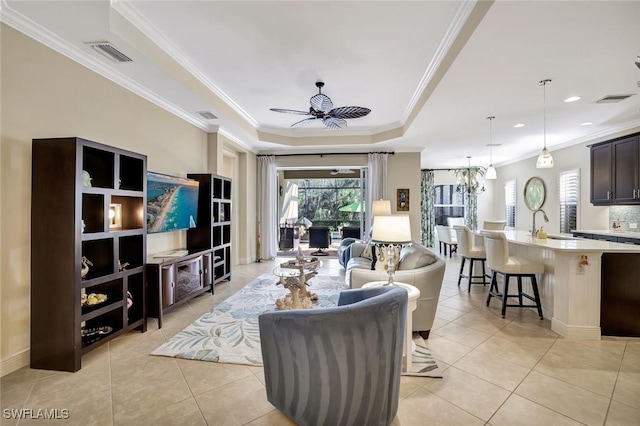 living room with light tile patterned floors, visible vents, a tray ceiling, and ornamental molding