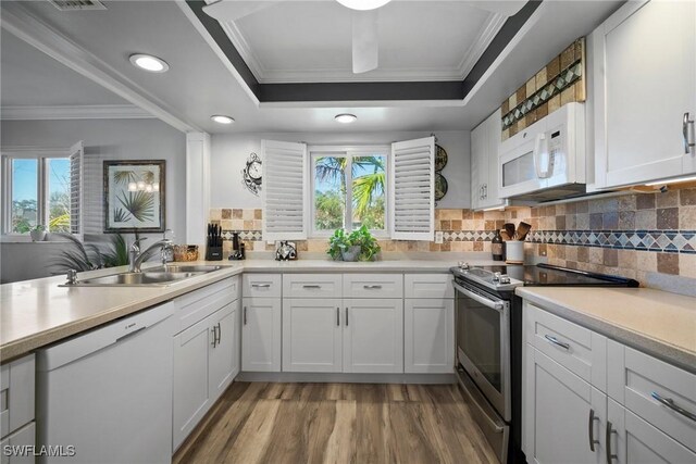 kitchen featuring tasteful backsplash, a tray ceiling, light wood-style floors, white appliances, and a sink