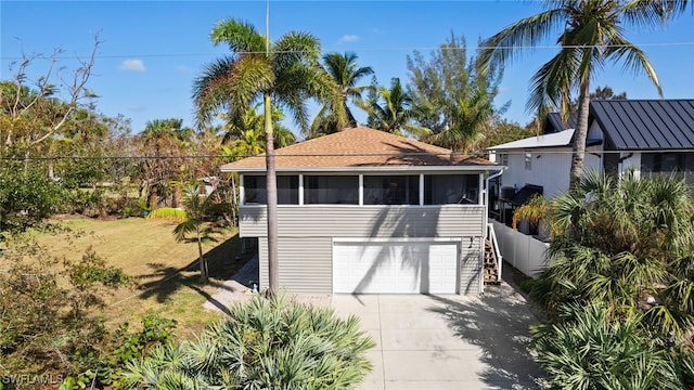 view of outdoor structure with a garage, fence, concrete driveway, and a sunroom