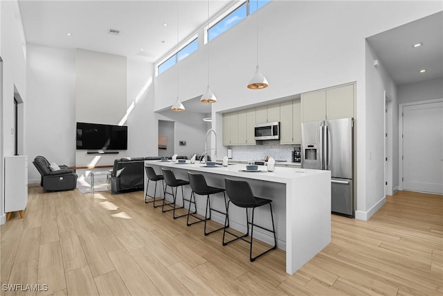 kitchen featuring light wood finished floors, a breakfast bar, appliances with stainless steel finishes, light countertops, and decorative backsplash