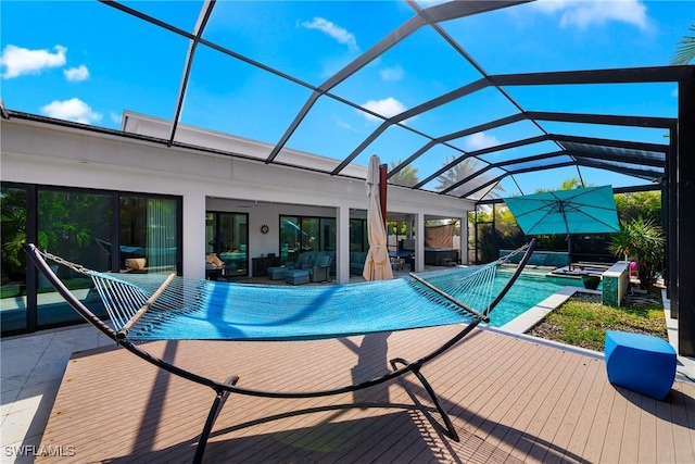 pool with glass enclosure, a wooden deck, a ceiling fan, and a hot tub