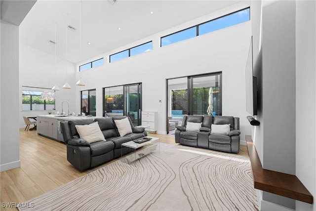 living room with light wood finished floors, plenty of natural light, baseboards, and a towering ceiling