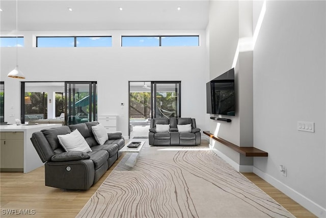 living area with light wood-type flooring, baseboards, and a towering ceiling