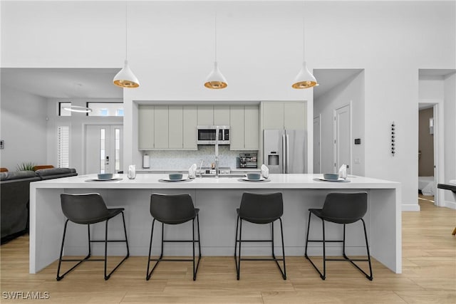 kitchen with tasteful backsplash, light wood finished floors, a breakfast bar area, gray cabinets, and appliances with stainless steel finishes