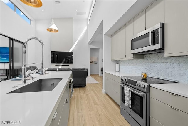 kitchen with open floor plan, light countertops, decorative backsplash, stainless steel appliances, and a sink