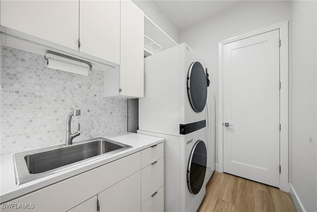 laundry area featuring cabinet space, light wood-style floors, stacked washer / drying machine, and a sink