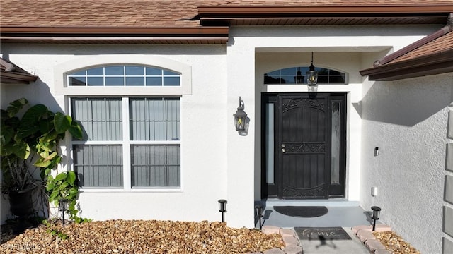 property entrance featuring stucco siding and a shingled roof