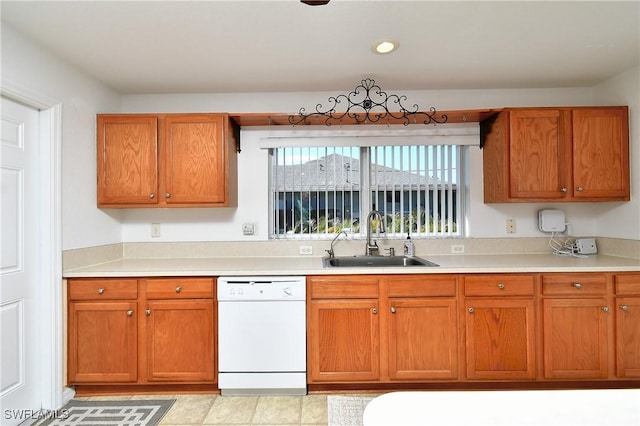 kitchen with a sink, brown cabinets, light countertops, and white dishwasher