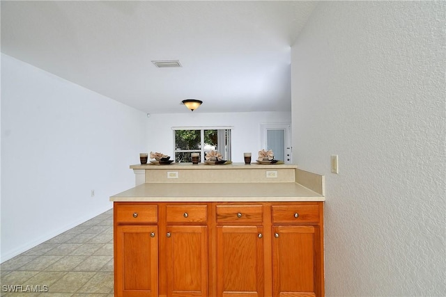 kitchen featuring a textured wall, visible vents, a peninsula, and light countertops